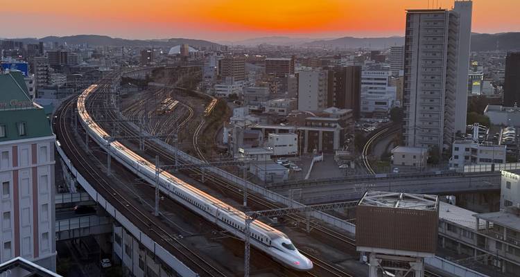 Bullet train moving through a city at sunset.