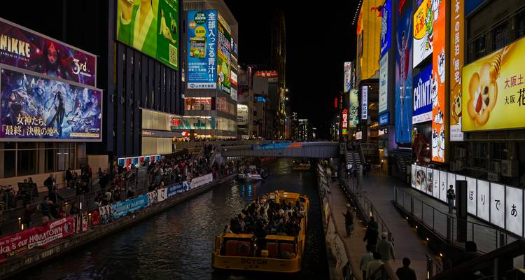 Busy street scene with illuminated signs and a canal.
