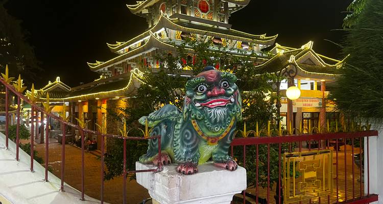 Façade colorée de temple illuminée la nuit avec une statue de lion.