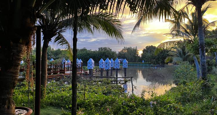 Vue panoramique d'un lac entouré de verdure et de petites huttes au coucher du soleil.