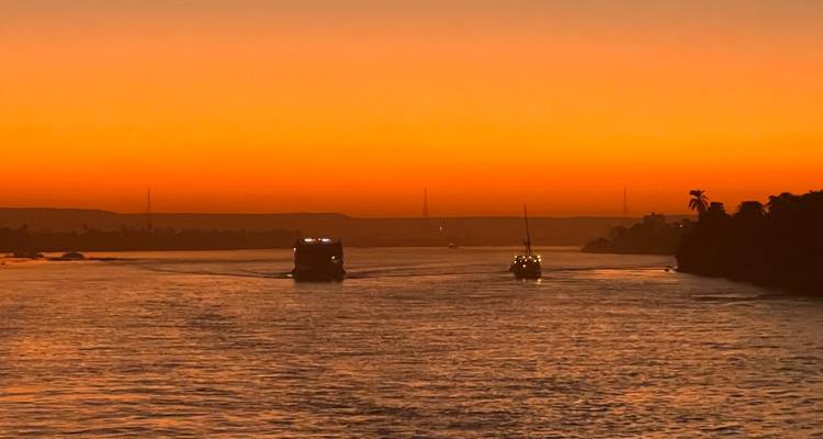 Una vibrante puesta de sol sobre un río, con botes silueteados contra el cielo naranja.