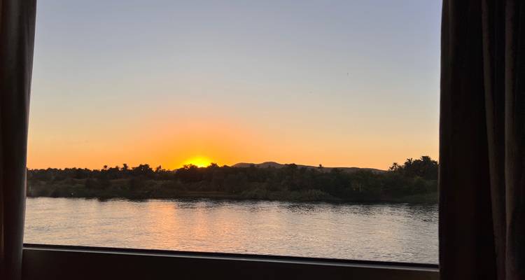 Vista escénica del río desde una ventana al atardecer con siluetas de árboles.