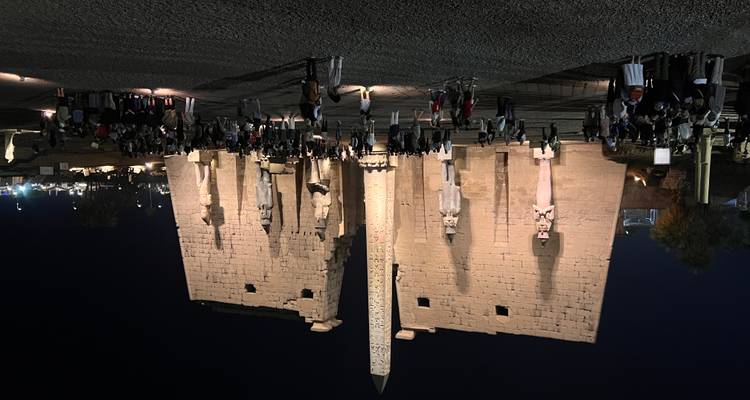 Vue nocturne d'un grand temple égyptien avec des touristes rassemblés.