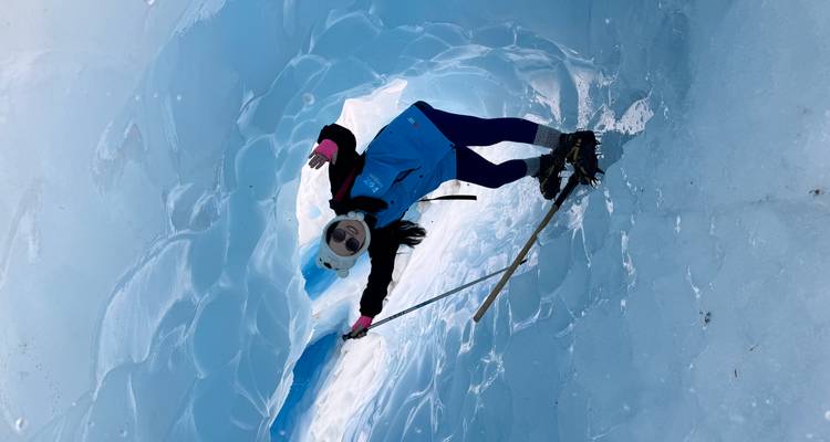 Persoon die een blauwe ijsgrot verkent met een ijsbijl