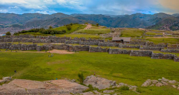 Extensas ruinas incas rodeadas de montañas con personas explorando.