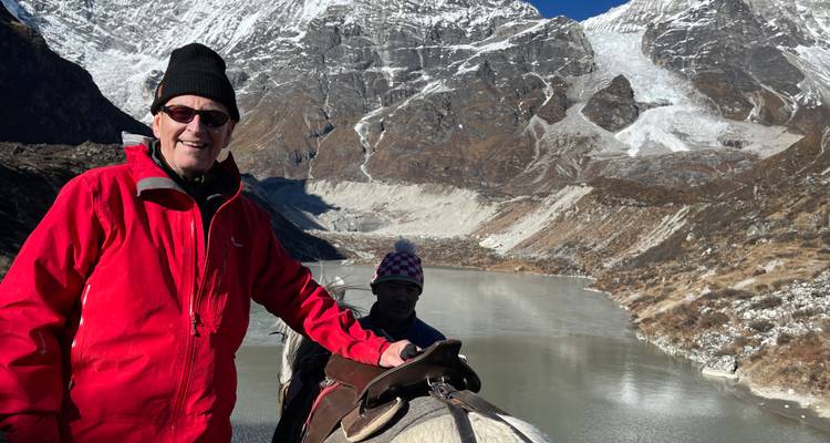 Deux personnes à cheval près d'un lac dans des montagnes enneigées.