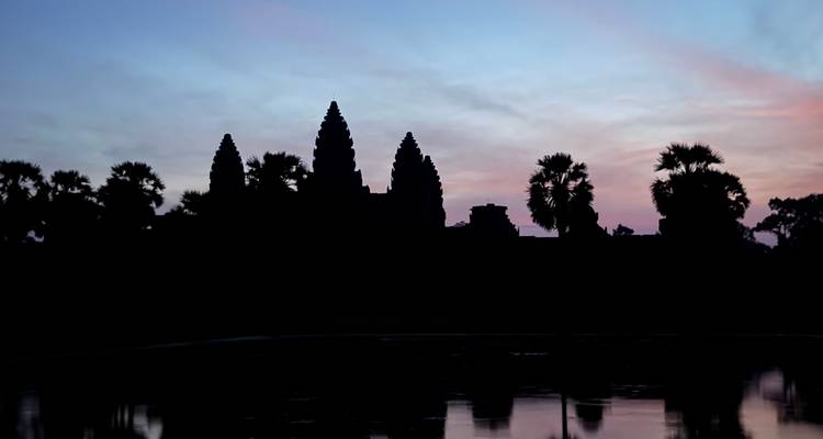 Silhouet van Angkor Wat bij zonsopgang, met een reflectie in een nabijgelegen waterpartij.
