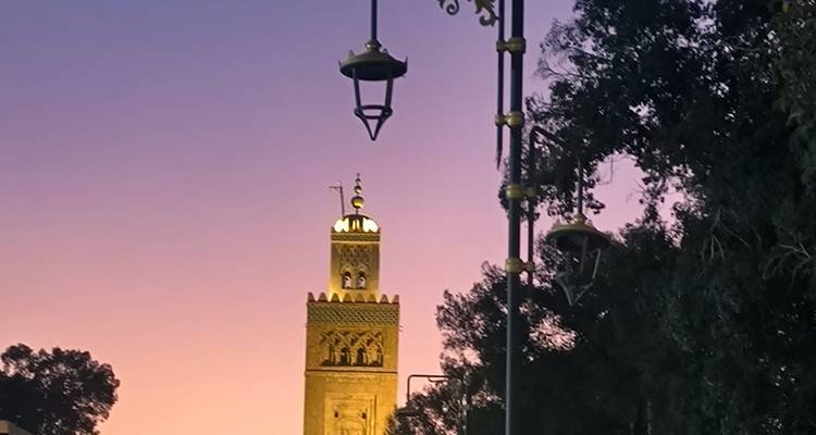 Minarett vor rosa Himmel mit Straßenlaternen im Vordergrund.