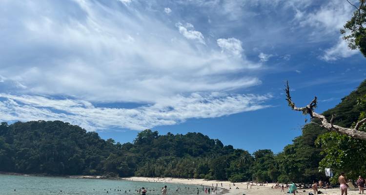 Een tropisch strandtafereel met mensen en blauwe lucht.