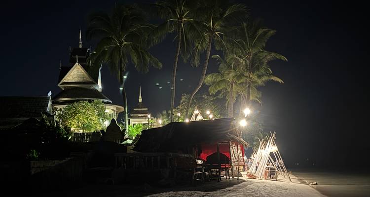 Strandrestaurant met palmbomen en nachtverlichting.