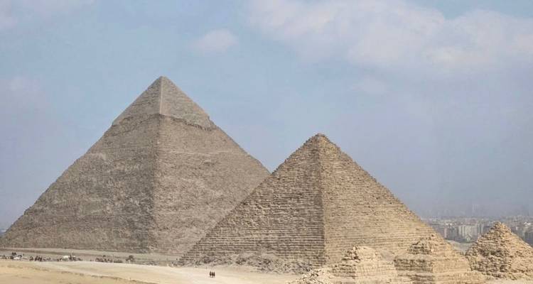 Dos pirámides se alzan en el desierto con una vista de la ciudad al fondo.