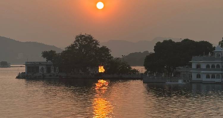 Zonsondergang boven een meer met reflecties en gesilhouetteerde architectuur.
