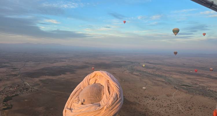Zahlreiche Heißluftballons am Himmel bei Sonnenaufgang über einer Wüstenlandschaft.