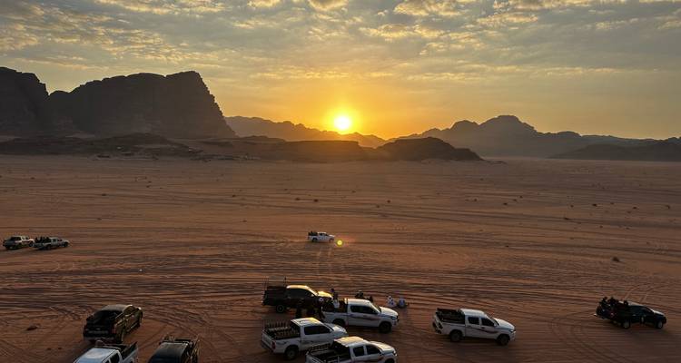 Paysage désertique avec des véhicules et un coucher de soleil en arrière-plan.