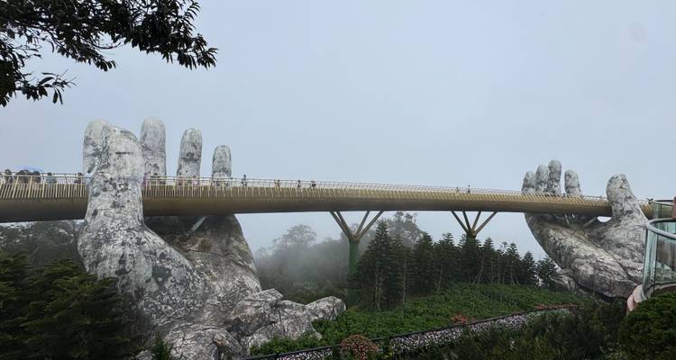 Escultura de manos grandes sosteniendo un puente peatonal entre la niebla.