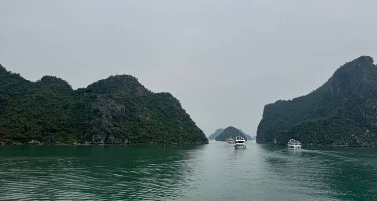Pasaje estrecho entre islas de piedra caliza con barcos bajo un cielo nublado.