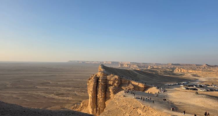 Rand van een woestijnklif met auto's en mensen die uitkijken over het landschap.