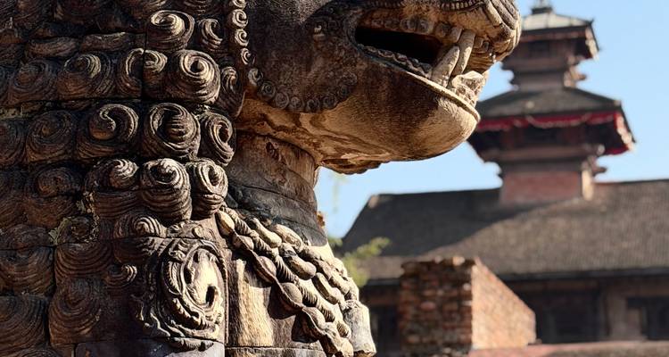 Nahaufnahme einer Löwenstatue mit traditioneller Architektur im Hintergrund.