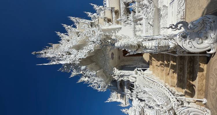 Weißer Tempel mit kunstvollen Schnitzereien und blauem Himmel.