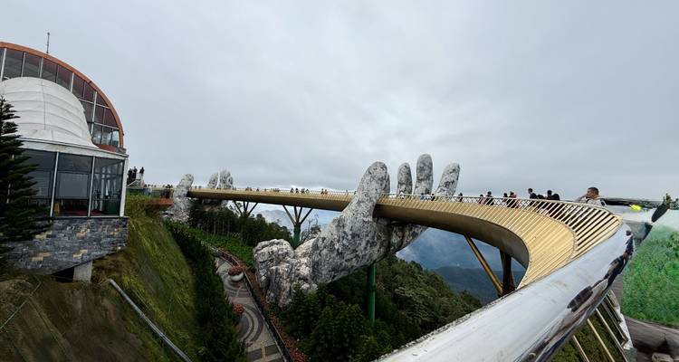 Puente dorado sostenido por manos gigantes de piedra con turistas.