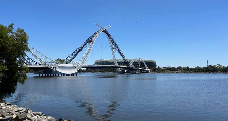 Pont moderne enjambant une rivière calme avec un stade en arrière-plan.