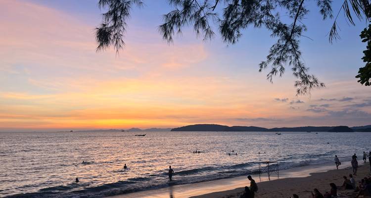 Playa durante la puesta de sol con personas nadando y relajándose.