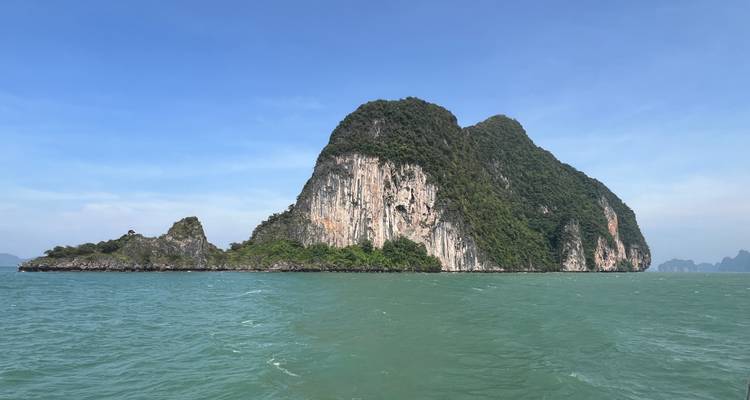 Une grande île rocheuse avec de la verdure entourée par l'océan sous un ciel bleu dégagé.