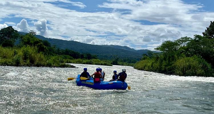Grupo de personas navegando en balsa por un río rodeado de montañas boscosas.