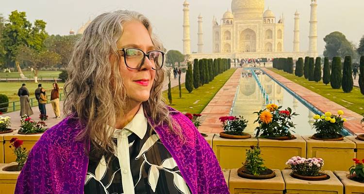 Persona posando frente al Taj Mahal con flores y sendero de jardín.