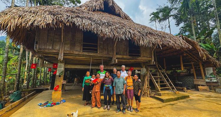 Groupe de personnes posant devant une maison traditionnelle au toit de chaume.