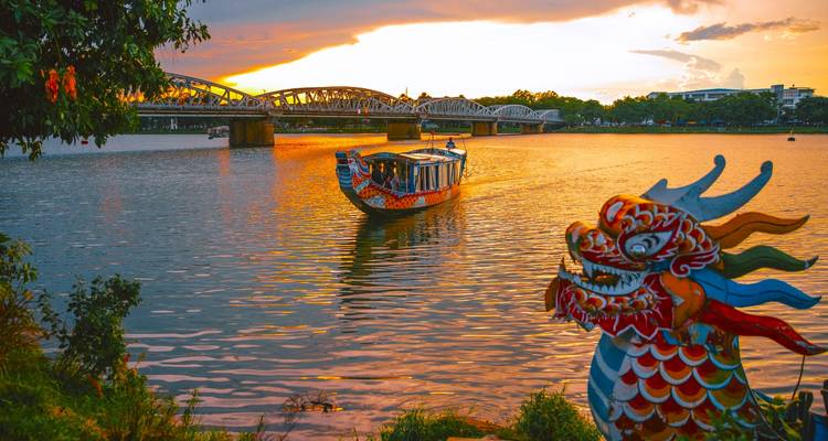 Bateau-dragon sur une rivière avec un pont et un ciel de coucher de soleil.