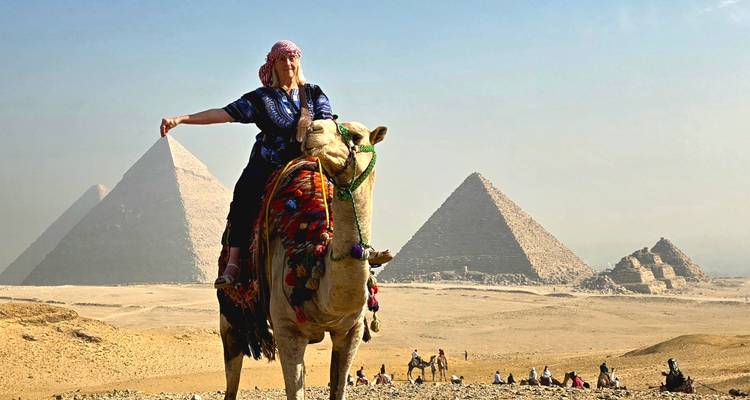 Personne à dos de chameau avec des pyramides en arrière-plan.