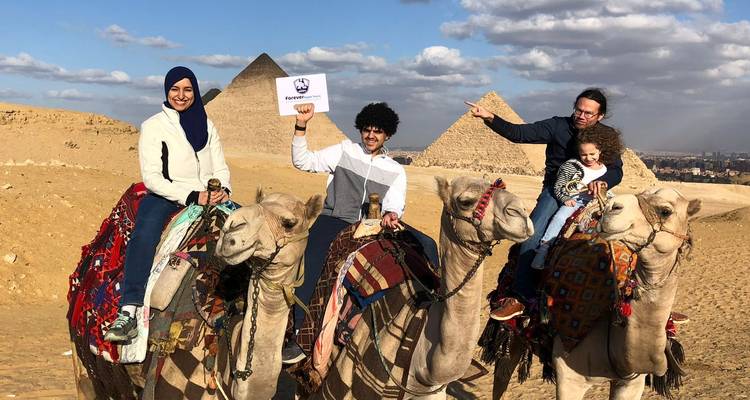 Vrolijke groep die kamelen berijdt bij piramides.