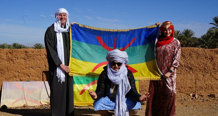 Tres personas con vestimenta tradicional sosteniendo una bandera colorida.