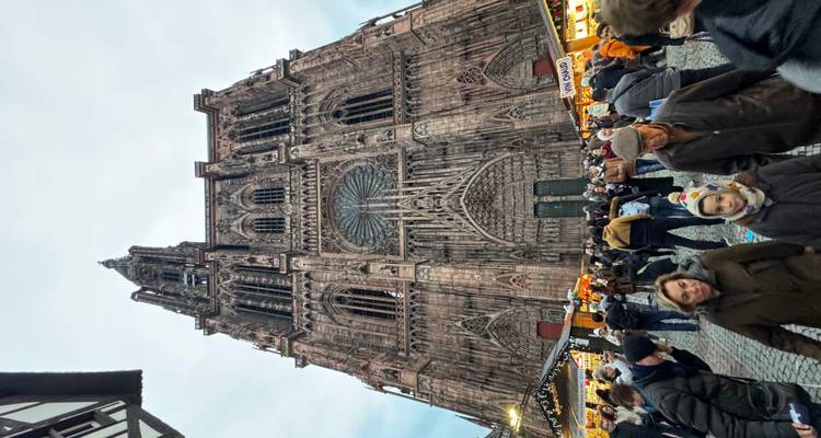 Een grote gotische kathedraal met ingewikkelde details en een menigte mensen ervoor, mogelijk een kerstmarkt.