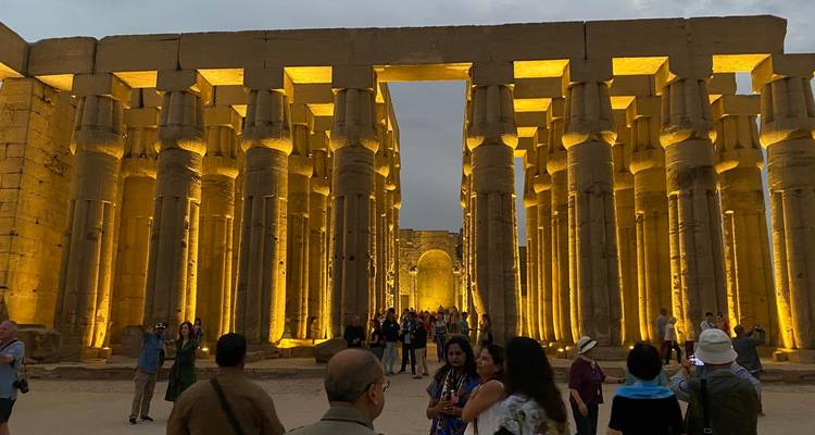 Touristes explorant un grand temple égyptien antique aux colonnes illuminées.