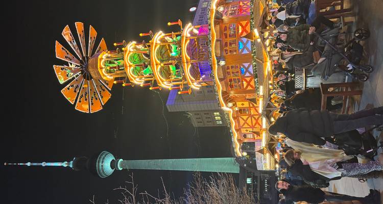 Scène de marché nocturne avec une grande décoration illuminée et une tour de télévision.