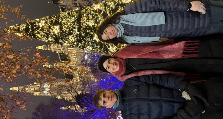 Trois personnes posant à un marché de Noël avec un sapin illuminé derrière elles.