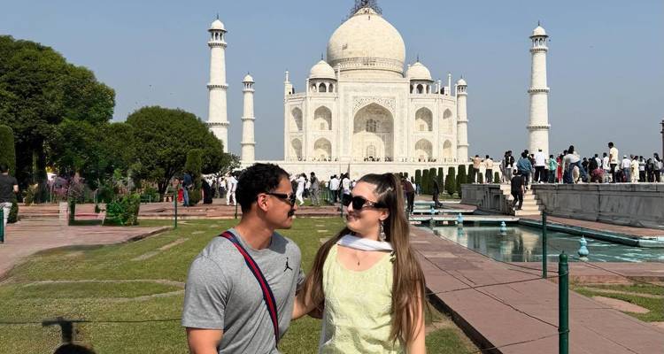 Couple souriant devant le Taj Mahal avec un ciel bleu clair.