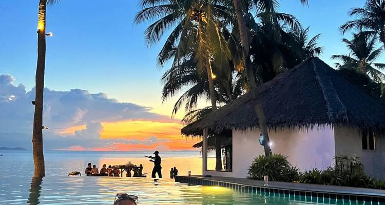 Des gens profitant d'une piscine avec vue sur un coucher de soleil tropical.