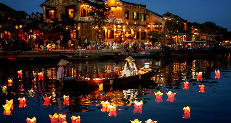Scène nocturne de Hoi An avec un bateau sur une rivière et des lanternes illuminées.
