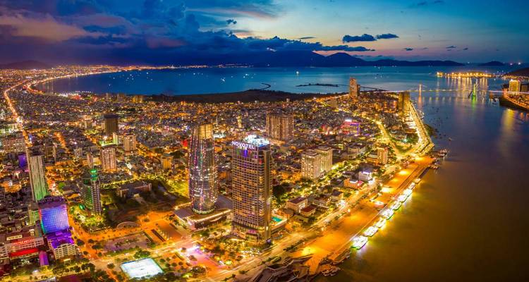 Vue aérienne d'une ville animée avec des bâtiments illuminés et un littoral au crépuscule.