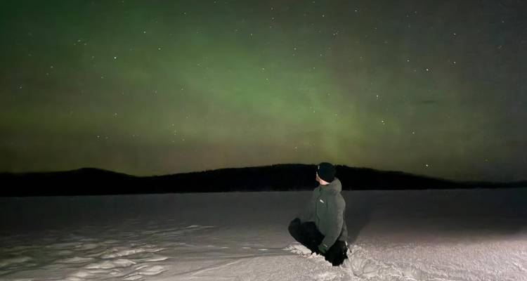 Persona sentada en la nieve observando la aurora boreal.