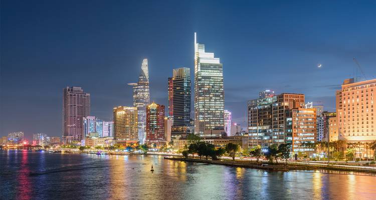 Vue nocturne d'un horizon urbain avec des bâtiments illuminés se reflétant sur une rivière.