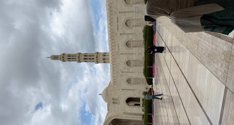 Vista exterior de una mezquita con un minarete alto y personas caminando.