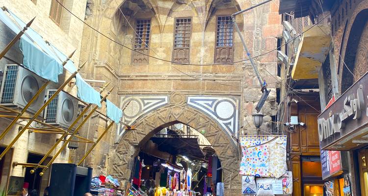 Scène de marché animée avec une arche de pierre ornée au-dessus.