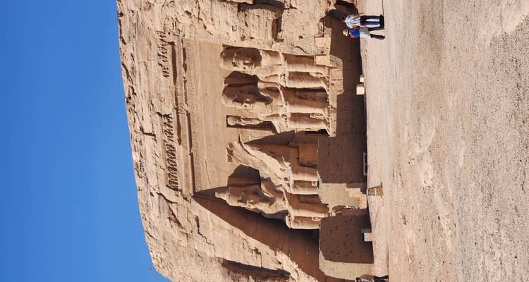 Grandes estatuas talladas en una roca con turistas explorando.