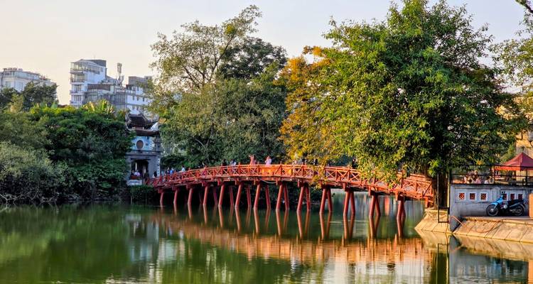 Le pont rouge emblématique de Hanoï au-dessus d'un lac calme avec des arbres verts et des bâtiments.