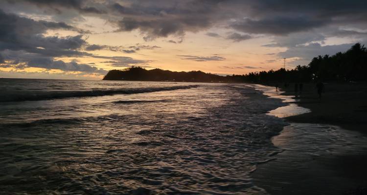 Beachfront at sunset with waves and silhouetted people.