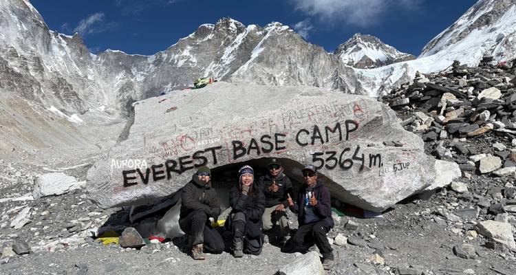 Grupo de personas posando frente a un letrero en un campamento base de montaña.